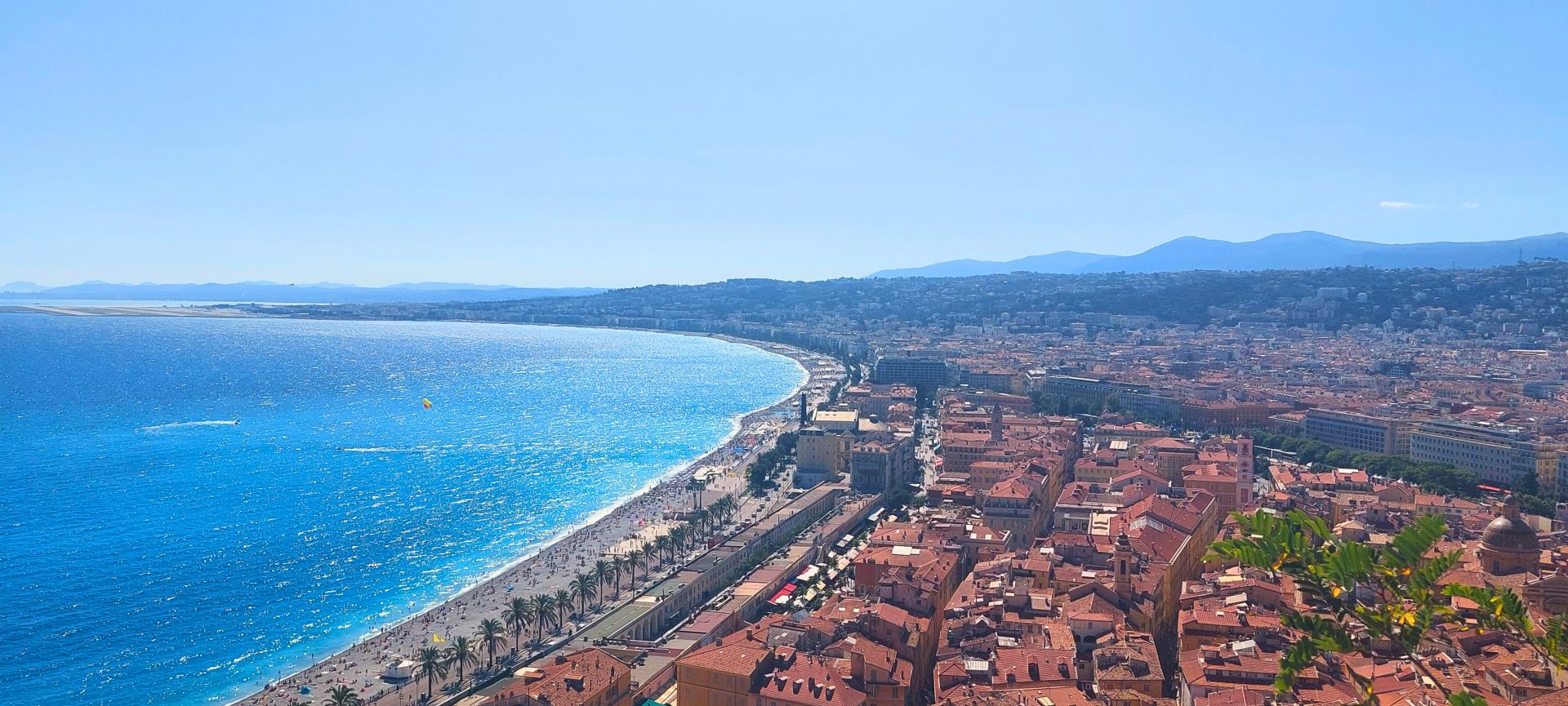 Panoramablick über die Altstadt von Nizza mit rotgedeckten Häusern, Palmenpromenade und türkisblauem Mittelmeer
