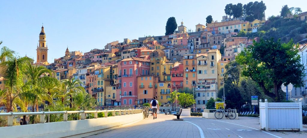 Blick auf die bunte Altstadt von Menton mit pastellfarbenen Häusern, Kirchturm und Palmen an der französischen Riviera – eines der schönsten Ziele für Tagesausflüge ab Nizza