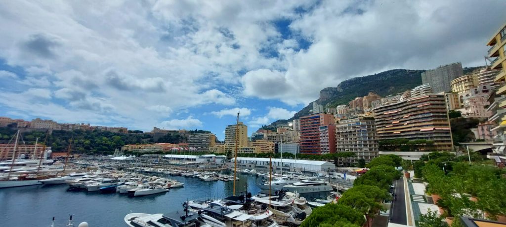 Panoramablick auf den Yachthafen von Monaco mit luxuriösen Booten, Hochhäusern und Bergen im Hintergrund