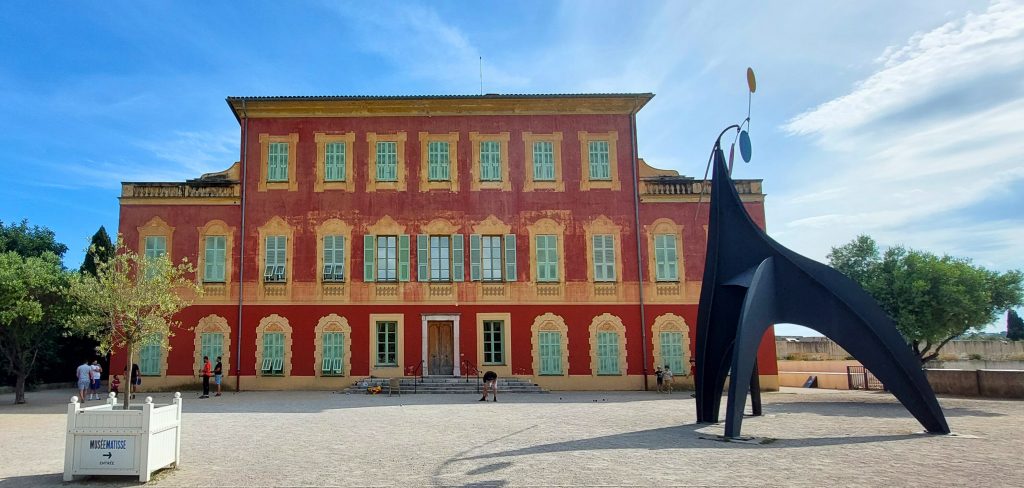 Musée Matisse in Nizza, historisches rotes Gebäude mit grünen Fensterläden und moderner Skulptur im Vordergrund