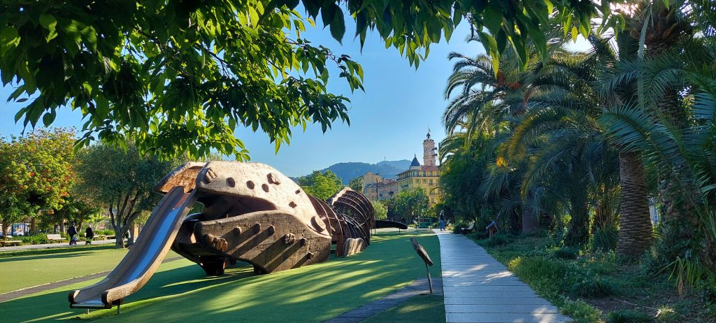 Promenade du Paillon in Nizza mit grünen Palmen, Spielplatz in Form eines Meeresdrachens und Blick auf die Altstadt