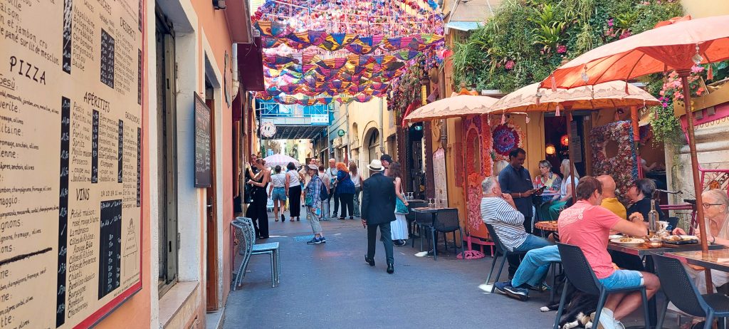Rue Droite in der Altstadt von Nizza mit bunten Häusern, Cafés, Straßendekorationen und Menschen in mediterraner Atmosphäre