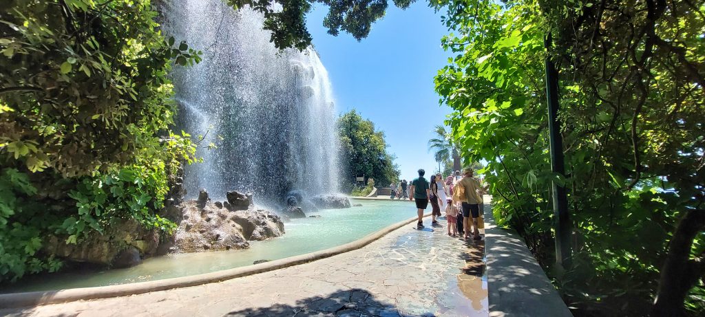 Wasserfall auf dem Colline du Château in Nizza, umgeben von grüner Natur mit Besuchern bei sonnigem Wetter