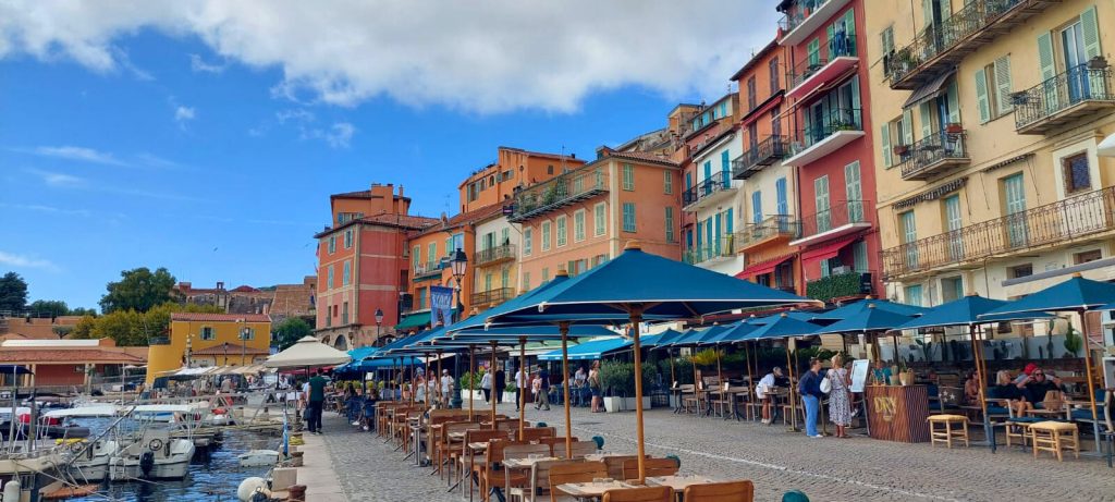 Charmante Hafenpromenade von Villefranche-sur-Mer mit bunten Häuserfassaden, Cafés und Booten im Mittelmeerhafen