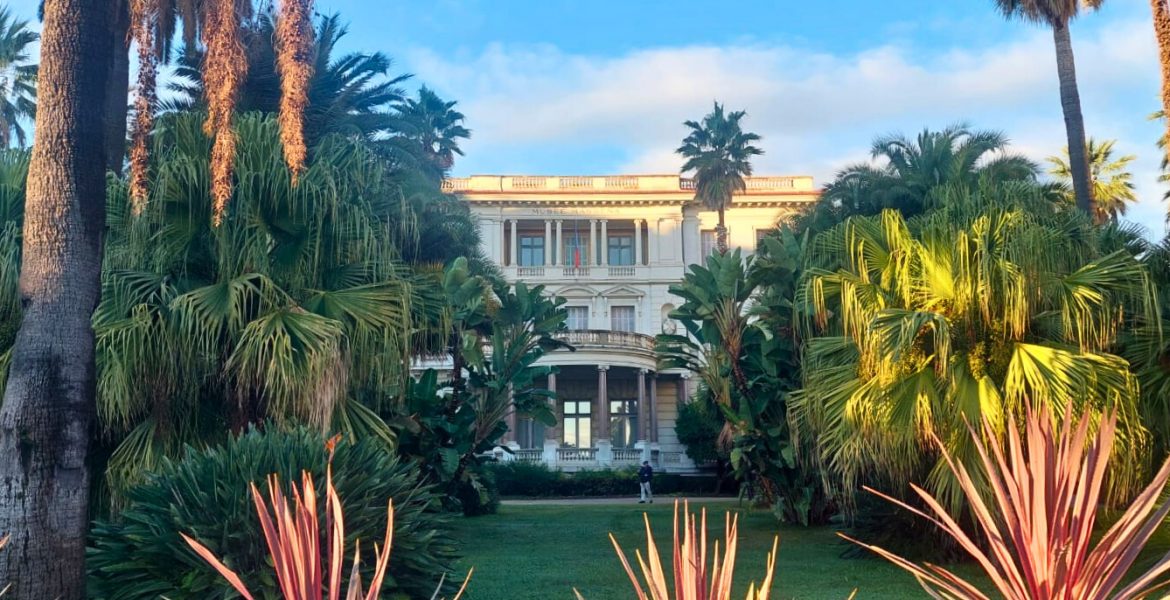Blick auf das Musée Masséna in Nizza, umgeben von Palmen und tropischen Pflanzen im Abendlicht.