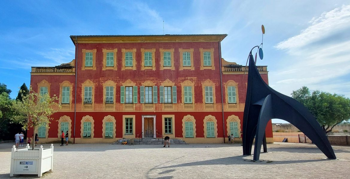 Musée Matisse in Nizza, historisches rotes Gebäude mit grünen Fensterläden und moderner Skulptur im Vordergrund